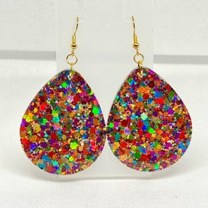 May include: A pair of teardrop-shaped earrings with a vibrant, multicolored glitter design. The earrings have gold-colored fish hook ear wires. The glitter includes shades of red, orange, yellow, green, blue, and purple.