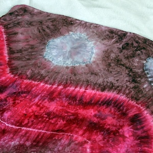 May include: A tie-dye fabric with a red, pink, and white swirl pattern. The fabric has two large, light gray circles with darker gray centers.