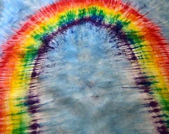 May include: A tie-dye fabric square with a rainbow arch design on a light blue background.