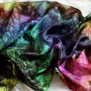 May include: A colorful silk scarf with a tie-dye pattern in shades of green, blue, purple, pink, and yellow. The scarf is draped over a white surface.