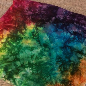 May include: A colorful tie-dye fabric with shades of red, purple, blue, green, and orange. The fabric has a swirling pattern and a soft, textured feel.