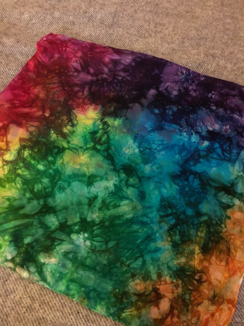 May include: A colorful tie-dye fabric with shades of red, purple, blue, green, and orange. The fabric has a swirling pattern and a soft, textured feel.