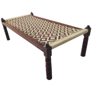 May include: A woven daybed with a geometric pattern in shades of brown and beige. The bed frame is made of dark wood, with decorative legs. The woven surface is tightly knit, creating a comfortable and stylish piece of furniture.