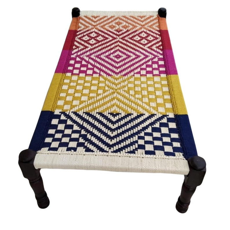 May include: A woven bed frame with a colorful geometric pattern. The bed features a rectangular design with dark wooden legs and a woven surface in shades of red, pink, yellow, and blue.