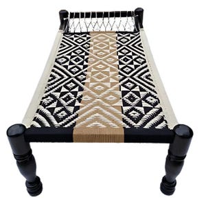 May include: A woven daybed with a geometric pattern in black, white, and tan. The bed frame is black with turned legs. The woven surface is approximately 72 inches long.