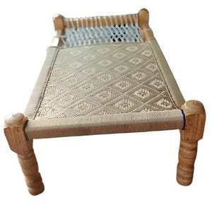 May include: A small, light-colored wooden bed frame with woven rope detailing. The bed features a woven surface and decorative wooden legs. The headboard and footboard are made of wood. The bed is designed for a small space.