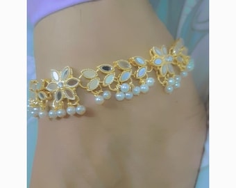 May include: A gold-toned anklet featuring floral and leaf-shaped elements with mirrored accents and dangling faux pearls. The anklet is designed with a delicate chain and is suitable for various occasions.