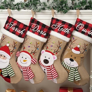 以下が含まれることがあります： サラ、ドリス、キース、オズウィンと名前が刺繍された4つのクリスマスストッキング。各ストッキングはジュート素材で、赤と黒のチェック柄のカフス、サンタ、雪だるま、ホッキョクグマ、トナカイのぬいぐるみキャラクターが特徴です。お祝いのクリスマスの装飾。