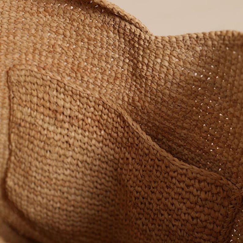 May include: Close-up of a woven bag made from natural fibers. The bag has a textured surface with a pocket detail. The color is a warm, earthy brown, suggesting a handmade or artisanal product. The weave is tight, indicating durability.