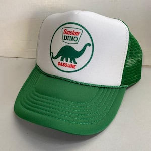 May include: Green and white trucker hat featuring the Sinclair Oil logo with a green dinosaur and the word "GASOLINE". The hat has a green brim and mesh back, with a white front panel.