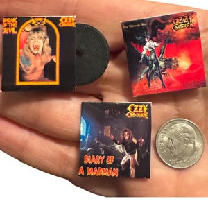 K&ouml;nnte beinhalten: Miniatur-Albumh&uuml;llen von Ozzy Osbourne. Die Alben umfassen "Speak of the Devil", "The Ultimate Sin" und "Diary of a Madman". Eine schwarze Schallplatte ist ebenfalls vorhanden. Eine M&uuml;nze dient als Gr&ouml;&szlig;enreferenz.