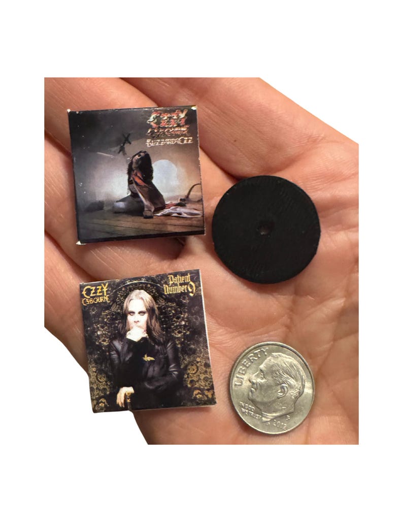 K&ouml;nnte beinhalten: Miniatur-Albumcover von Ozzy Osbournes Alben "Blizzard of Ozz" und "Patient Number 9". Eine schwarze Scheibe und eine M&uuml;nze sind ebenfalls vorhanden. Die Albumcover zeigen Albumkunst und Text. Die M&uuml;nze dient zum Gr&ouml;&szlig;envergleich.