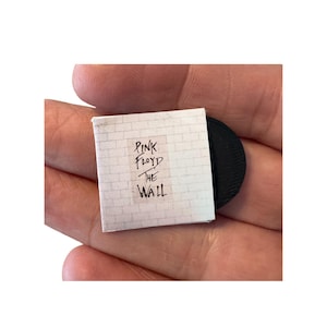 May include: Miniature album cover for Pink Floyd's "The Wall" with a black vinyl record. The album cover is white with a brick wall design and the album title and band name in black text. The record is black.