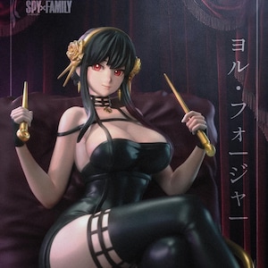 May include: A detailed figure of a character from "Spy x Family." The figure is of a woman with black hair, red eyes, and a black dress. She is holding two golden objects. The figure is seated on a purple surface.