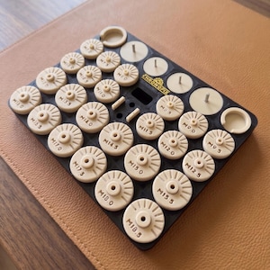 Puede incluir: Una bandeja organizadora rectangular negra con la etiqueta Chronofix que contiene numerosos componentes circulares de color crema con ranuras radiales y marcas de tamaño de M7.0 a M18.5, además de ranuras circulares vacías y tres pasadores.