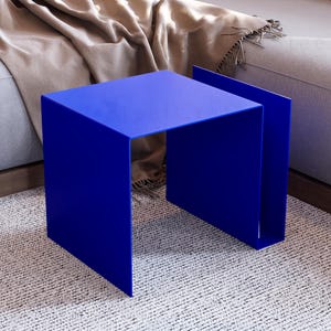 Peut inclure: Une table d'appoint moderne bleu cobalt, de forme carrée et au design minimaliste. La table mesure environ 40 cm de large, 40 cm de profondeur et 40 cm de haut. Elle est posée sur un tapis texturé blanc cassé, près d'un canapé gris.
