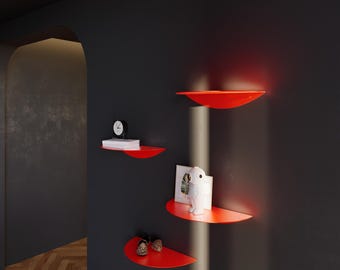 Puede incluir: Estanterías de pared rojas semicirculares montadas en una pared gris oscuro. Exhiben un reloj, libros, una figura blanca y zapatos decorativos. Un elemento de diseño moderno.