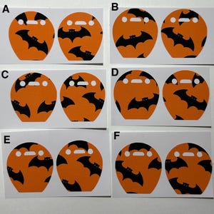 May include: Orange and black Halloween-themed stickers featuring a bat pattern. Each sticker has a unique bat arrangement. The stickers are die-cut with a small rectangular opening at the top, perfect for crafting or decorating.