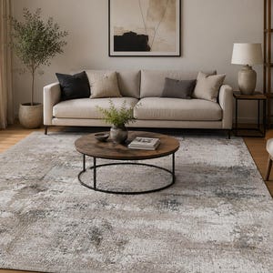 Peut inclure: Un grand tapis rectangulaire présentant un motif abstrait vieilli dans des tons beige, gris et blanc. Le tapis a un aspect texturé avec des variations de couleurs mouchetées sur toute la surface, recouvrant le sol devant un canapé beige.