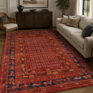 Op de afbeelding: Een rechthoekig vloerkleed met een dieprood en marineblauw kleurenpalet, voorzien van een centraal rasterpatroon en een rand versierd met herhalende motieven van paarden en ruiters, dat de vloer in een woonkamer bedekt.
