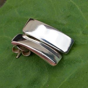 Minimalist sterling silver rectangular stud earrings on green leaf background