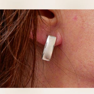 Small sterling silver rectangular stud earring worn on ear close-up