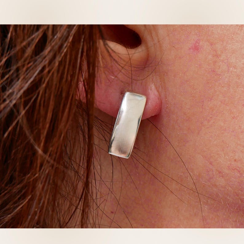 Small sterling silver rectangular stud earring worn on ear close-up