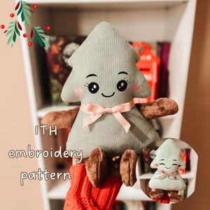 May include: A plush toy shaped like a Christmas tree with a textured sage green fabric body, brown limbs, and a light pink ribbon tied around its center. The face features embroidered black eyes, eyelashes, a smile, and pink heart-shaped cheeks. Text reads ITH embroidery pattern.