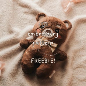 Könnte beinhalten: Ein brauner Plüsch-Teddybär mit gestickten Gesichtszügen, einschließlich großer dunkler Augen und rosa Wangen, der eine cremefarbene Schleife um den Hals trägt. Der Text ITH embroidery pattern FREEBIE! ist über den Brustbereich des Bären gelegt.