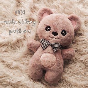 Könnte beinhalten: Ein altrosa Plüschteddybär mit gestickten schwarzen Augen samt Wimpern, einer kleinen schwarzen Nase und einem aufgestickten Mund. Der Bär trägt eine schwarz-weiß karierte Gingham-Schleife am Hals und hat einen runden Flicken auf dem Bauch. Text: ITH embroidery pattern.