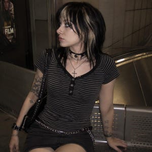 May include: A short-sleeved henley top featuring horizontal black and grey stripes, a black button placket, and a V-neckline. The top is worn with a black skirt, a black shoulder bag, a layered necklace with a cross pendant, and a choker.