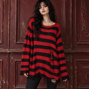 May include: A long-sleeved, oversized jumper featuring horizontal red and black stripes. The knit garment has a distressed, ripped texture with frayed edges along the hem, neckline, and a prominent vertical tear on the lower front panel.