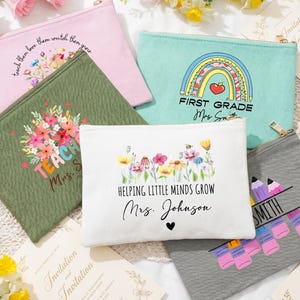 Könnte beinhalten: Eine Sammlung von Reißverschlusstaschen in verschiedenen Farben, darunter Rosa, Grün, Weiß und Grau. Jede Tasche hat einzigartige Designs und Texte, wie Blumenarrangements, Regenbogen und Lehrer-Themen.