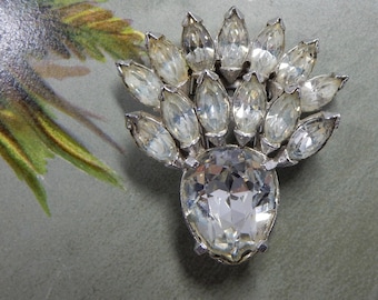 May include: A silver-toned brooch featuring a large, central pear-shaped clear crystal at the base, topped with a fan-shaped arrangement of twelve marquise-cut clear crystals set in a metallic frame with prong settings.