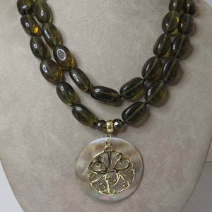 May include: A double strand necklace made of dark green oval beads with a large, round, mother-of-pearl pendant featuring a gold filigree design.