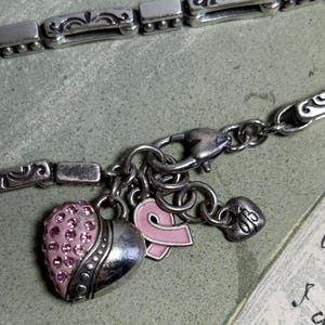 Peut inclure: Bracelet &agrave; breloques argent&eacute; avec un charm en forme de c&oelig;ur orn&eacute; de strass roses, un charm ruban rose et un petit charm c&oelig;ur. Le bracelet a un fermoir mousqueton et des maillons d&eacute;coratifs.