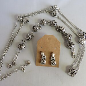 May include: A silver necklace with a chain and decorative balls, a matching bracelet, and a pair of silver earrings.