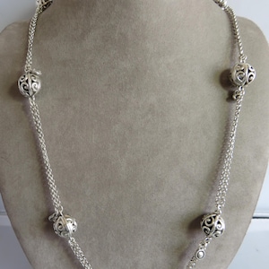 May include: A silver necklace with a double chain and five decorative, openwork, round charms. The charms are evenly spaced along the chain.