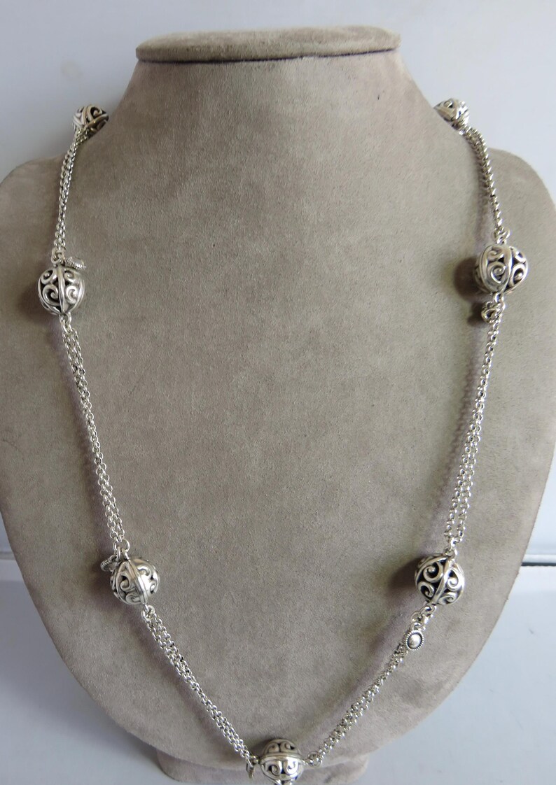 May include: A silver necklace with a double chain and five decorative, openwork, round charms. The charms are evenly spaced along the chain.