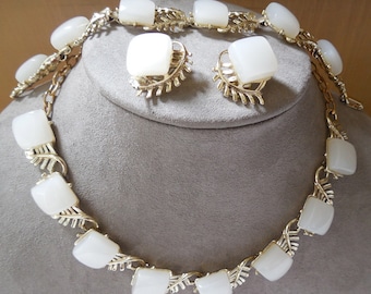 May include: A gold-tone metal necklace and matching clip-on earring set featuring smooth, square-shaped white cabochon stones. The necklace links and earring settings are designed with a textured, leaf-like pattern connecting each white stone.