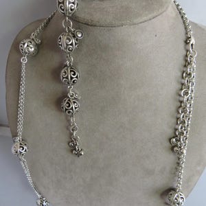 May include: A silver necklace with a delicate chain and decorative ball charms. The necklace is paired with matching silver earrings with a similar design.