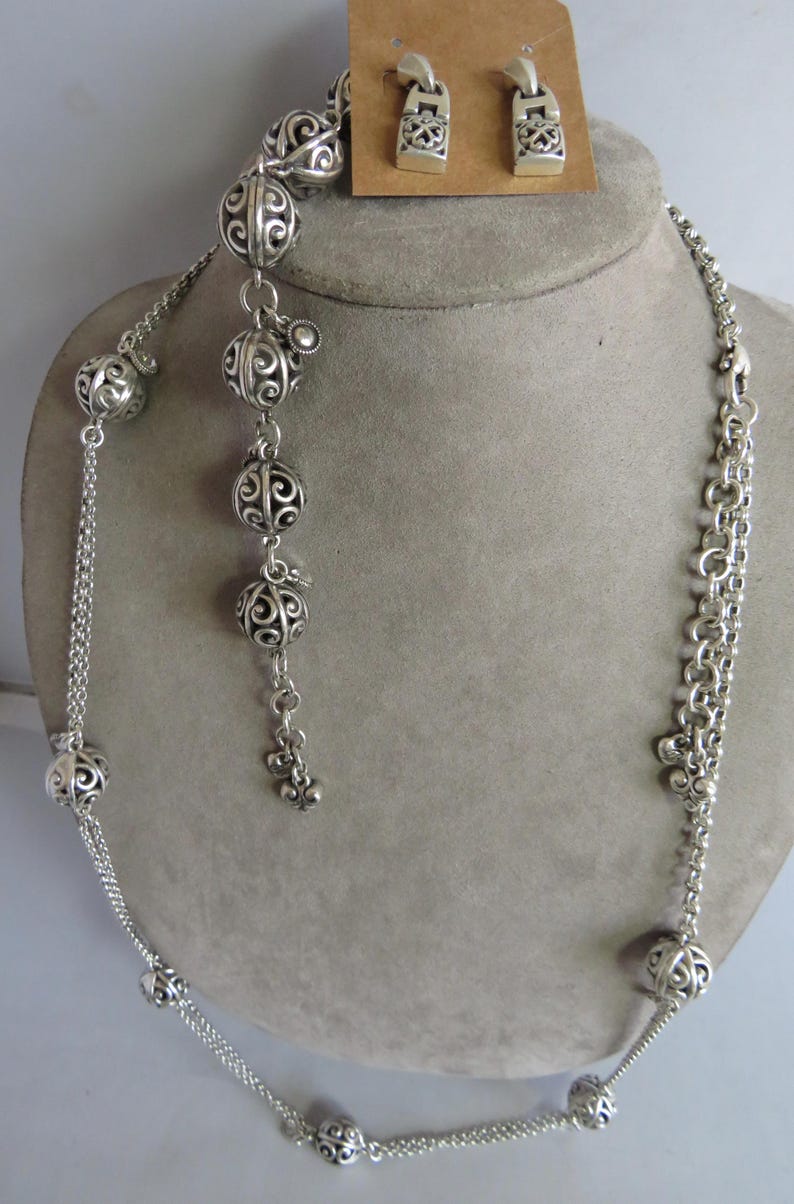 May include: A silver necklace with a delicate chain and decorative ball charms. The necklace is paired with matching silver earrings with a similar design.