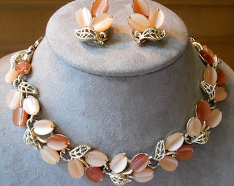 May include: A gold-tone metal necklace and matching clip-on earring set featuring clusters of oval-shaped, translucent peach and amber-coloured cabochons arranged like petals, interspersed with textured, leaf-shaped metal accents throughout.