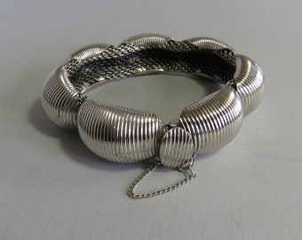 May include: A silver bracelet with a chain closure. The bracelet is made of a series of connected, rounded, ridged pieces.