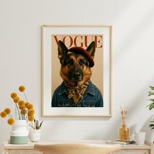 Op de afbeelding: Een ingelijste kunstdruk met een Duitse herder die een donkerrode baret, een sjaal met luipaardprint en een blauw spijkerjack draagt. Het woord VOGUE staat in grote rode letters bovenaan de beige achtergrond achter de hond gedrukt.