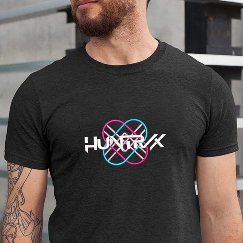 Puede incluir: Camiseta gris oscuro con el texto blanco "HUNTRX" y un logotipo rosa y azul ne&oacute;n. El logotipo es un dise&ntilde;o abstracto con formas entrelazadas. La camiseta tiene mangas cortas y cuello redondo.