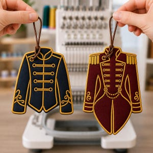 May include: Two embroidered ornaments shaped like military-style jackets. One is dark navy blue with gold trim and horizontal toggles. The other is deep burgundy with gold epaulets, toggles, and a decorative chain detail. Both have brown hanging loops.