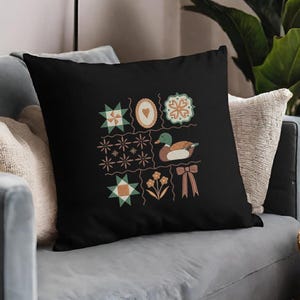 May include: Black decorative throw pillow featuring a patchwork design with various shapes and a duck illustration. The design includes stars, flowers, hearts, and a bow in shades of green, orange, and brown.