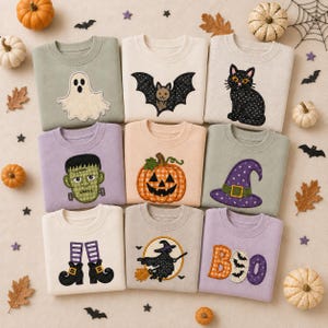 May include: Nine crewneck sweatshirts featuring embroidered Halloween designs including a ghost, bat, black cat, Frankenstein monster, pumpkin, witch hat, witch boots, witch on a broomstick, and the word BOO with bat silhouettes inside the letters.