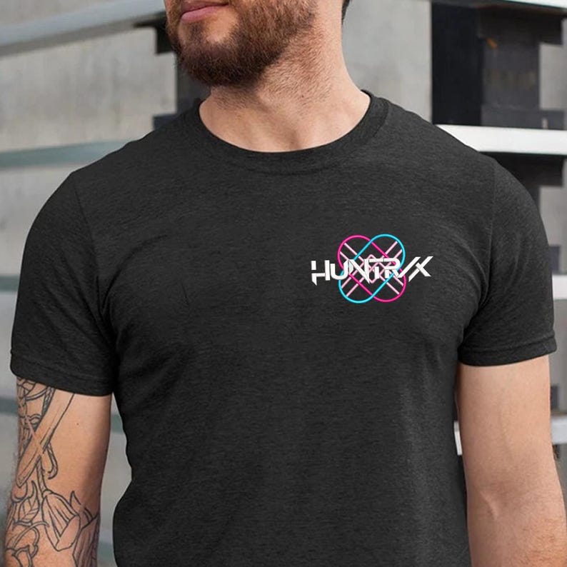 Puede incluir: Camiseta gris oscuro con cuello redondo. La camiseta presenta un logotipo en la parte superior izquierda del pecho. El logotipo es una marca denominativa blanca con la palabra "HUNTIRX" y un dise&ntilde;o geom&eacute;trico en rosa y azul.